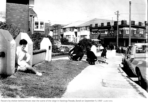 Passers-by shelter behind fences near the scene of the siege in Hastings Parade, Bondi on September 9, 1969Credit: Laurie Shea